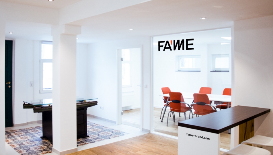 Modernes, helles Büro mit Fame-Branding und einem Konferenzraum mit orangefarbenen Stühlen.